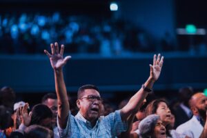 Diverse group of people engaging in worship with hands raised indoors.