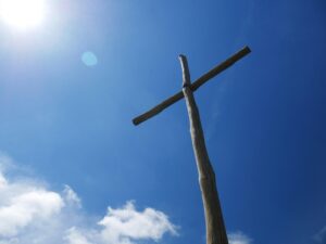 Low angle view of a wooden cross under a clear blue sky with bright sunlight.