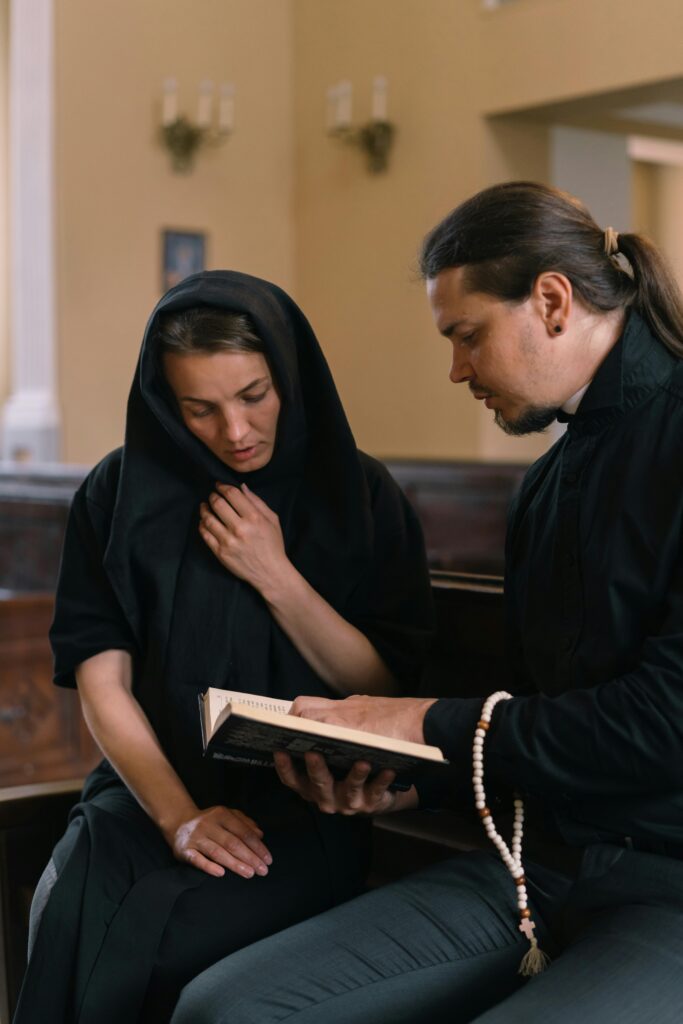 A man and woman in black attire engaged in a spiritual reading with prayer beads indoors.